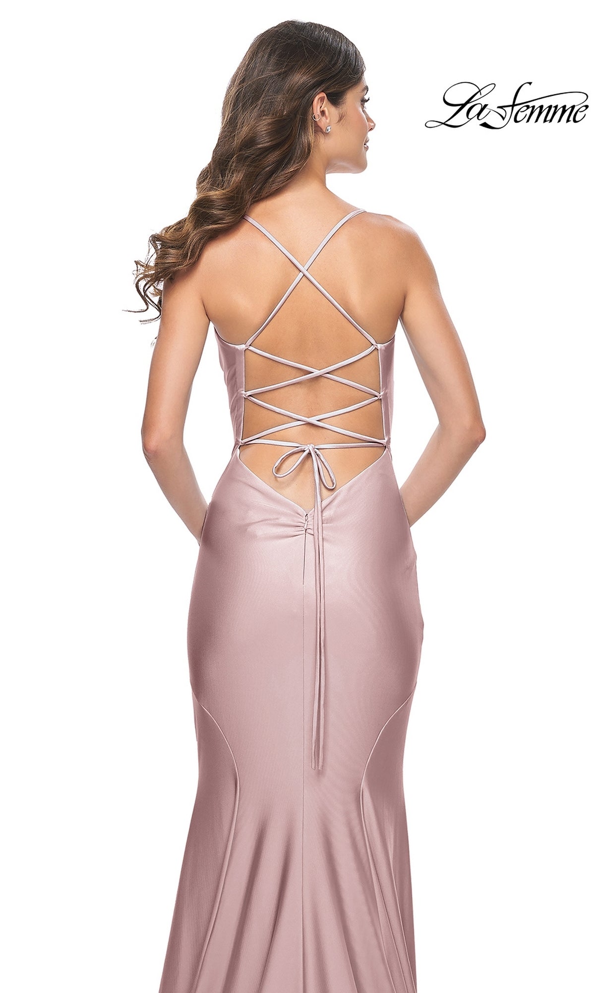 A woman wearing the La Femme Open-Back Long Prom Dress 31878 in blush pink satin, featuring spaghetti straps and a lace-up open back, stands against a white background with the